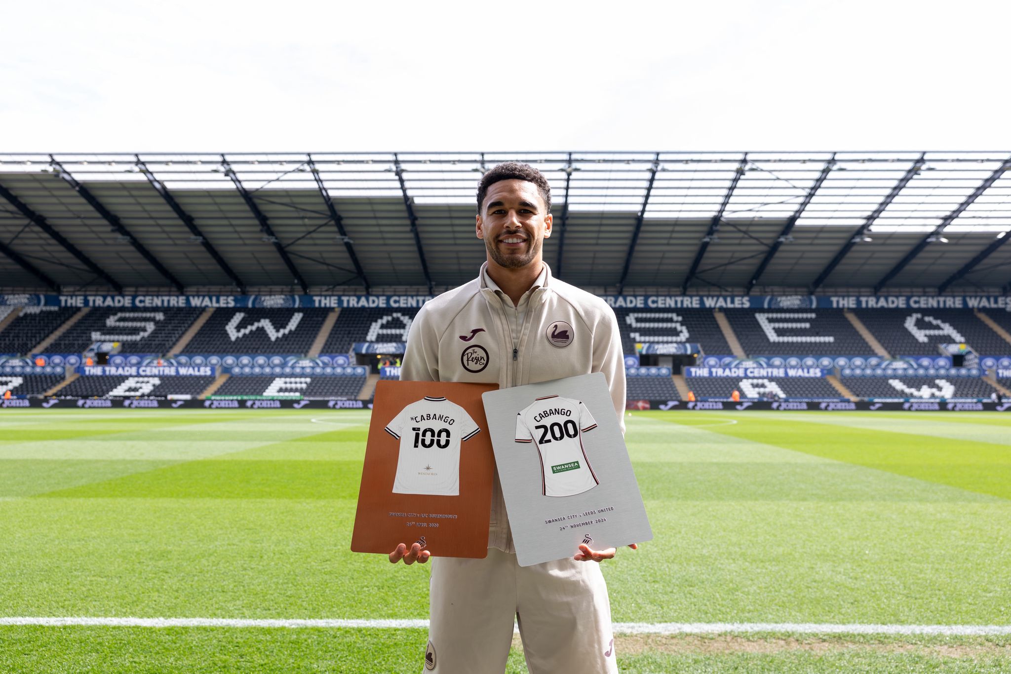 Ben Cabango holding both his 100 and 200 appearance plaques together on the pitch at the Swansea.com Stadium