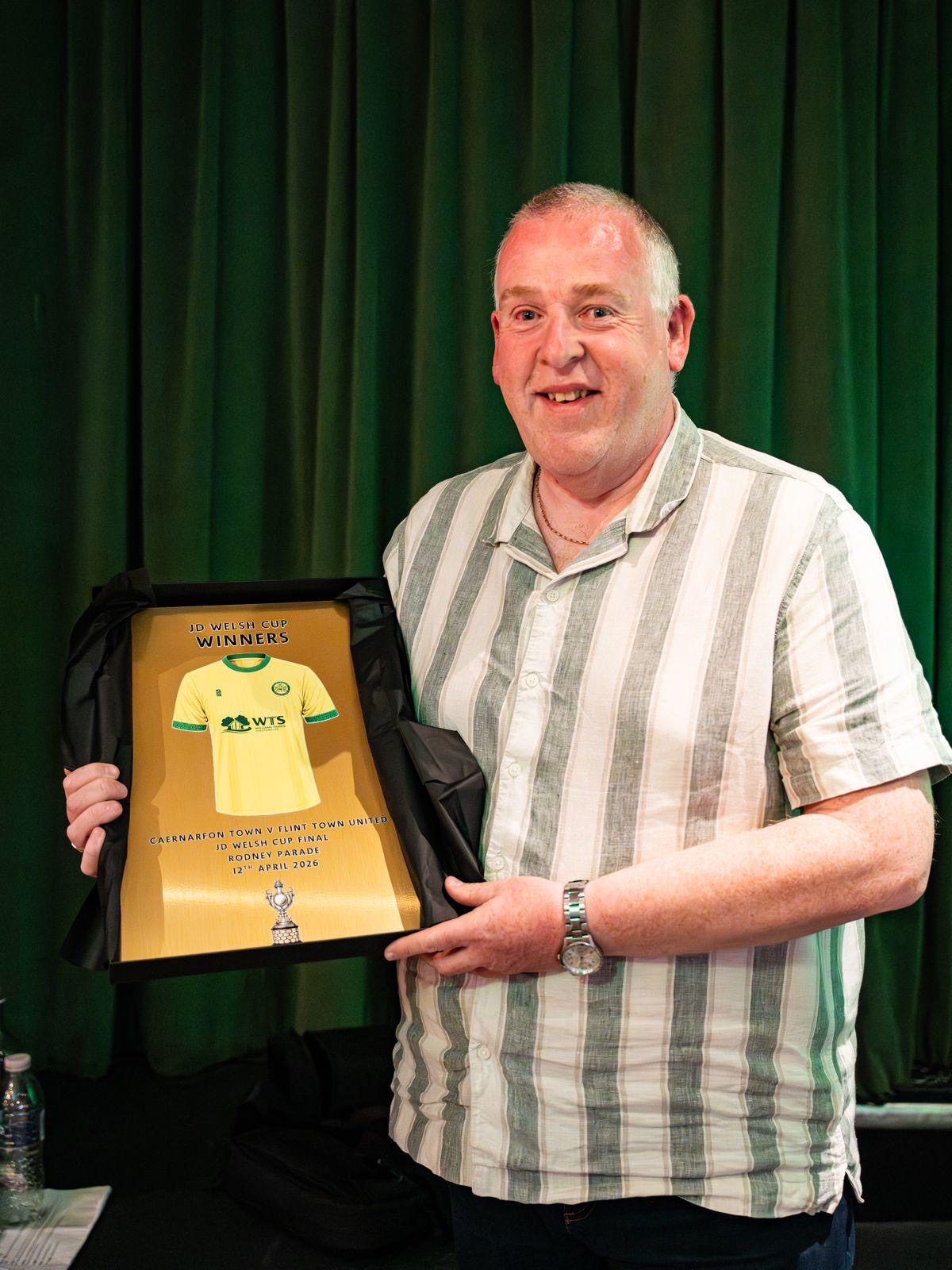 A Caernarfon Town FC director holding the JD Welsh Cup Winners plaque at an awards dinner