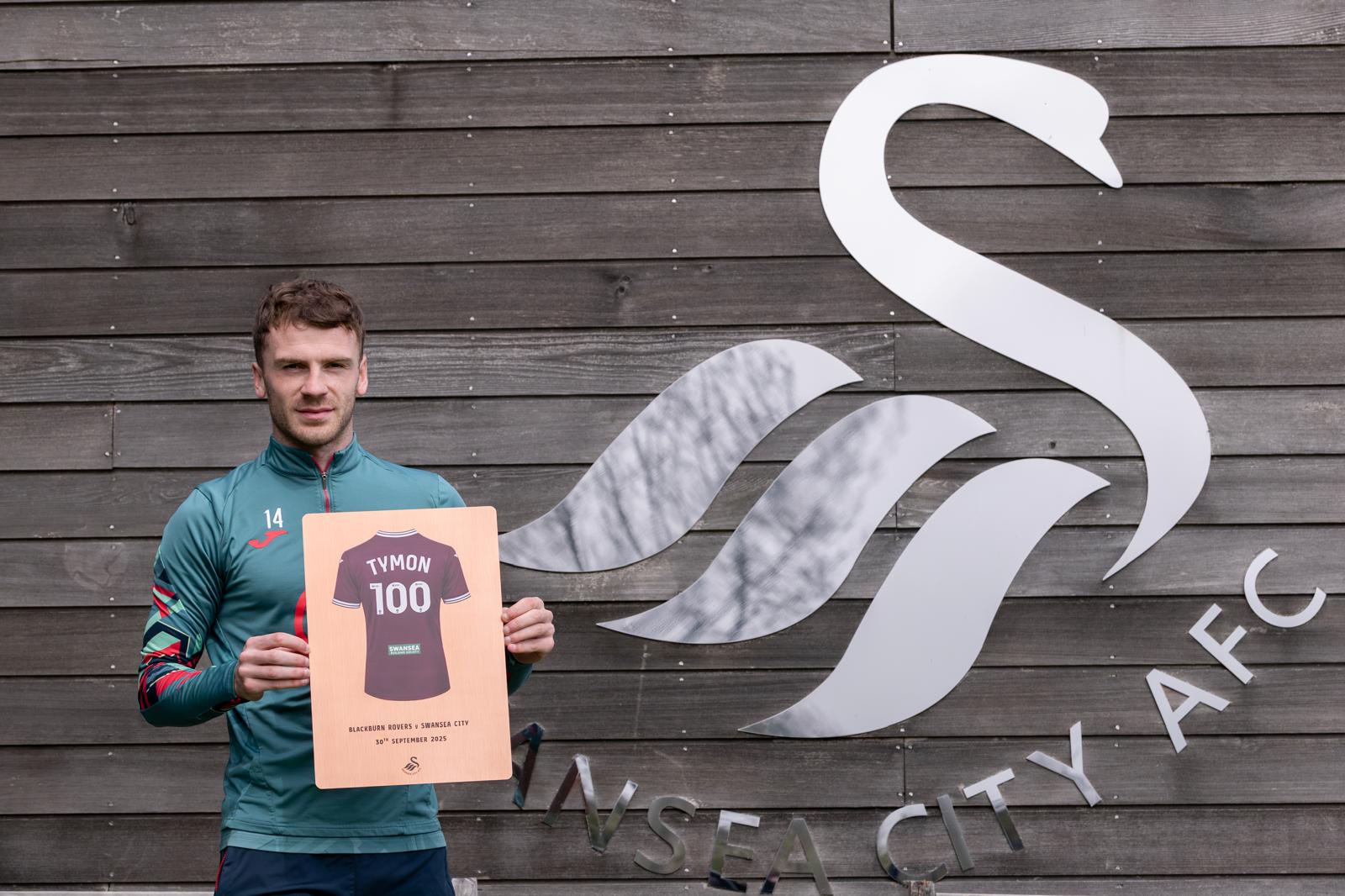 Josh Tymon holding his 100 appearance Copper finish plaque in front of the Swansea City AFC swan logo